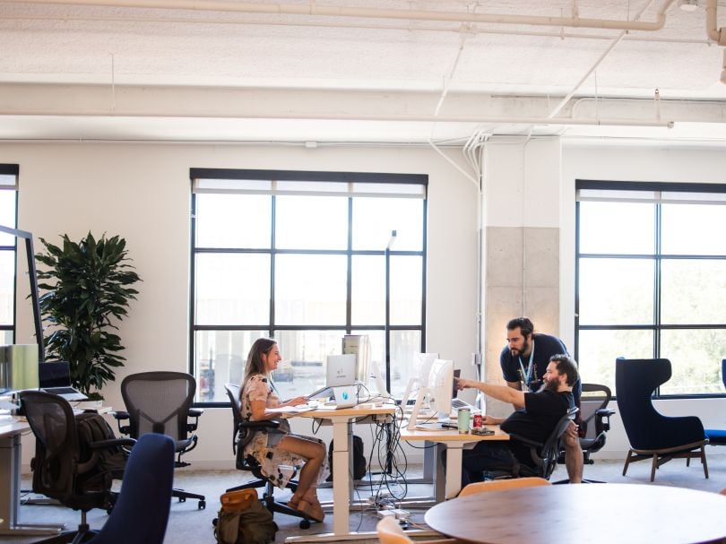Two Atlassian colleagues look at information on a computer monitor while their colleague works at a computer across from them